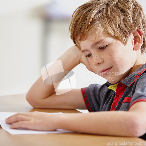 Image of Class, notebook and bored boy at desk, learning and education with school exam. Reading book, studying for test and child student in classroom with knowledge and thinking with depression on project.