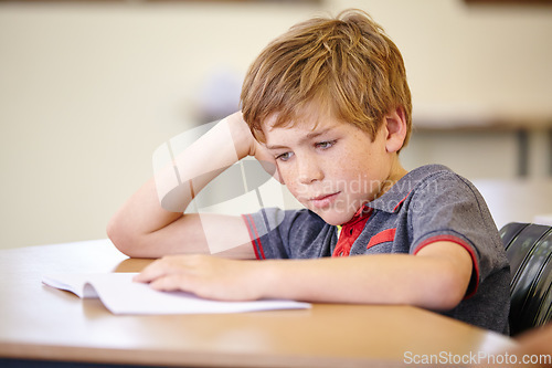 Image of Class, book and bored child at desk, learning and education with school exam. Reading notebook, studying for test and boy student in classroom with knowledge and thinking with depression on project.