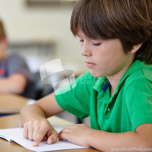 Image of Classroom, notebook and child at desk, reading and education for learning at school exam. Book, studying for test and boy student in classroom with knowledge and thinking with depression on project.