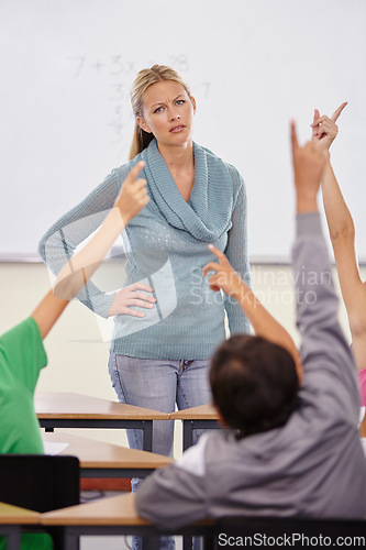 Image of Teacher woman, children group and raised hand in classroom for question, answer or pop quiz with stress. Teaching person, school kids and education with frustrated face, talking or lecture at academy