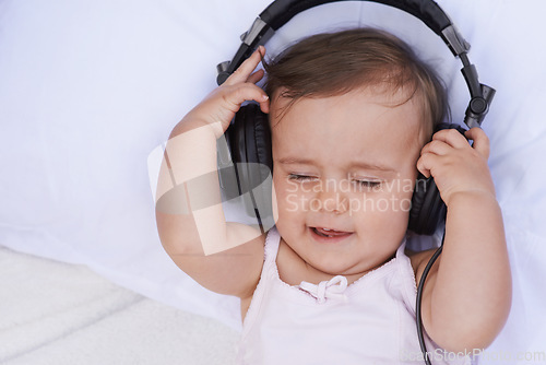 Image of Baby, headphones and streaming music to relax, radio and listening to podcast on bed at home. Girl, kid and hearing sound for child development or learning, toddler and calming playlist for audio