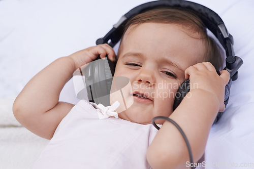 Image of Baby, headphones and listening to music for fun, streaming radio and podcast on bed at home. Child, relax and hearing sound for child development or learning, toddler and calming playlist for audio