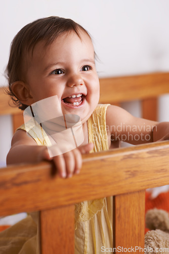 Image of Excited baby in crib, playing with smile and fun in home, child development and care in home. Toddler girl in cot with playful face, energy and happiness in cute kids bedroom, nursery or apartment.