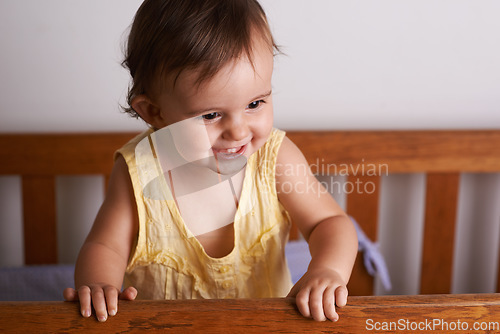 Image of Baby in crib, playing with smile and fun in home, child development and care in home. Excited toddler girl in cot with playful face, energy and happiness in cute kids bedroom, nursery or apartment