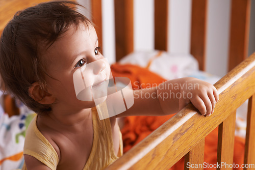 Image of Baby girl in crib, playing with smile and fun in home, child development and care in home. Toddler in cot with playful face, energy and happiness in cute kids bedroom, nursery or apartment at bedtime