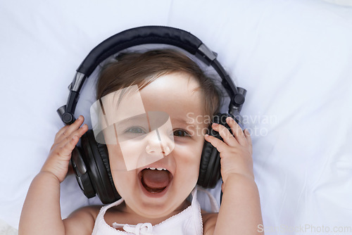 Image of Baby, headphones and music in portrait and singing, streaming radio and podcast on bed at home. Girl, relax and hearing audio for child development or learning, toddler and fun playlist for kid