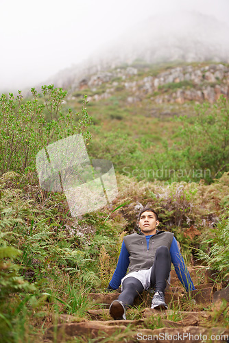 Image of Tired, runner and man on break in nature training, cardio exercise and endurance workout for wellness. Sports, fitness fatigue or healthy athlete resting in forest or uphill mountain trail outdoors