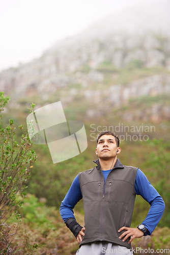 Image of Man, hiking and earphones for music, mountain and thinking for adventure, exercise or workout. Hiker, fitness and young for training, forest and nature to explore, hobby and heart health in outdoors