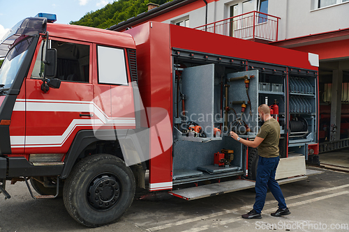 Image of A dedicated firefighter preparing a modern firetruck for deployment to hazardous fire-stricken areas, demonstrating readiness and commitment to emergency response