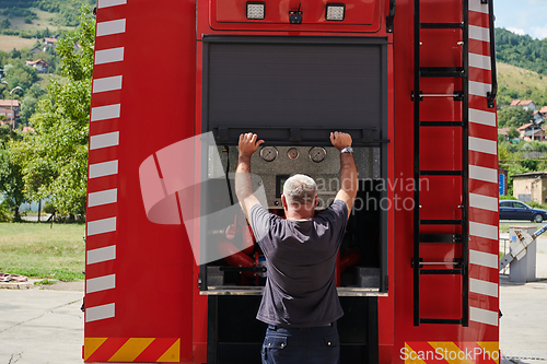 Image of A dedicated firefighter preparing a modern firetruck for deployment to hazardous fire-stricken areas, demonstrating readiness and commitment to emergency response