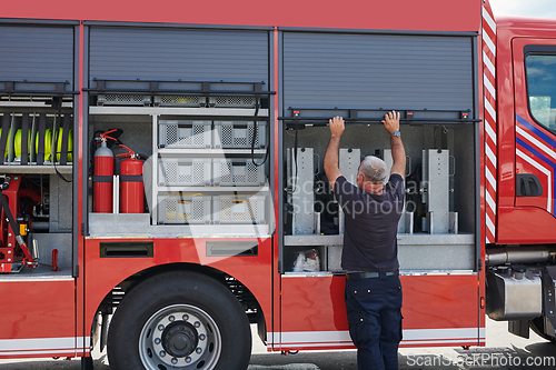 Image of A dedicated firefighter preparing a modern firetruck for deployment to hazardous fire-stricken areas, demonstrating readiness and commitment to emergency response