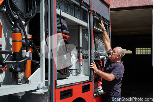 Image of A dedicated firefighter preparing a modern firetruck for deployment to hazardous fire-stricken areas, demonstrating readiness and commitment to emergency response