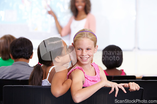 Image of Kids, classroom and whisper in ear for secret, gossip or communication in lesson at school. Little girl, students or friends listening to rumor, information or surprise in class together with teacher