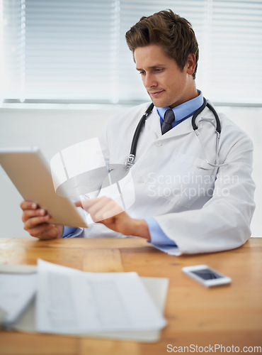Image of Tablet, research and doctor reading in his office for diagnosis or treatment at medical hospital. Internet, digital technology and professional young male healthcare worker sitting by desk in clinic.