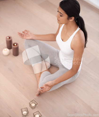 Image of Woman, calm meditation and spiritual in a home with candles and chakra for balance and mindfulness. Morning, wellness and zen in house on floor to relax for breathing and peace in lotus position