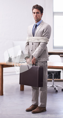 Image of Portrait of businessman in workplace tied up in rope with depression, control and sad in law firm. Serious attorney, lawyer or legal consultant bound in office, corporate hostage with bag and stress.