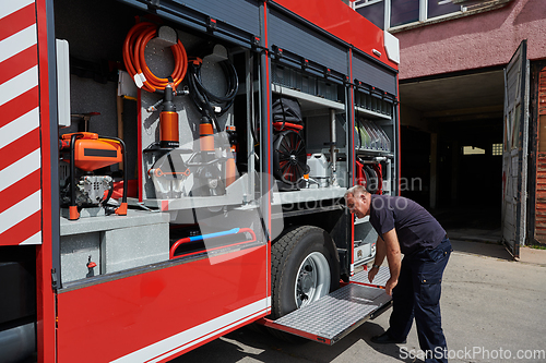 Image of A dedicated firefighter preparing a modern firetruck for deployment to hazardous fire-stricken areas, demonstrating readiness and commitment to emergency response