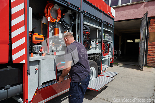 Image of A dedicated firefighter preparing a modern firetruck for deployment to hazardous fire-stricken areas, demonstrating readiness and commitment to emergency response