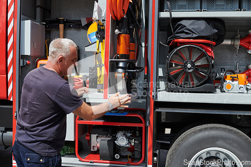 Image of A dedicated firefighter preparing a modern firetruck for deployment to hazardous fire-stricken areas, demonstrating readiness and commitment to emergency response