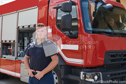 Image of A confident firefighter strikes a pose in front of a modern firetruck, exuding pride, strength, and preparedness for emergency response