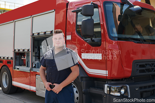 Image of A confident firefighter strikes a pose in front of a modern firetruck, exuding pride, strength, and preparedness for emergency response