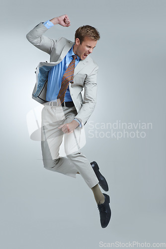 Image of Businessman, celebration and jumping for success in studio, winner and fist pump for triumph. Male person, professional and victory or accomplishment, cheering and energy or bonus by gray background