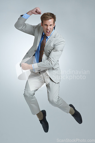 Image of Businessman, celebration and jumping for achievement in portrait, studio and fist pump for triumph. Male person, professional and victory or success, cheering and energy or win by gray background
