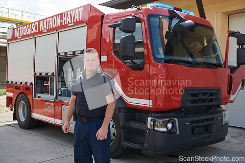 Image of A confident firefighter strikes a pose in front of a modern firetruck, exuding pride, strength, and preparedness for emergency response