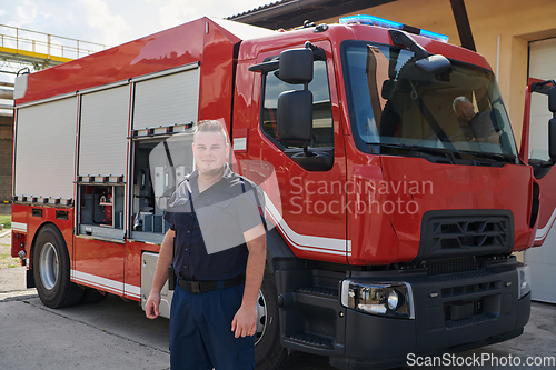Image of A confident firefighter strikes a pose in front of a modern firetruck, exuding pride, strength, and preparedness for emergency response