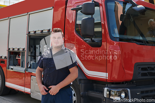 Image of A confident firefighter strikes a pose in front of a modern firetruck, exuding pride, strength, and preparedness for emergency response