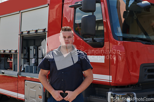 Image of A confident firefighter strikes a pose in front of a modern firetruck, exuding pride, strength, and preparedness for emergency response