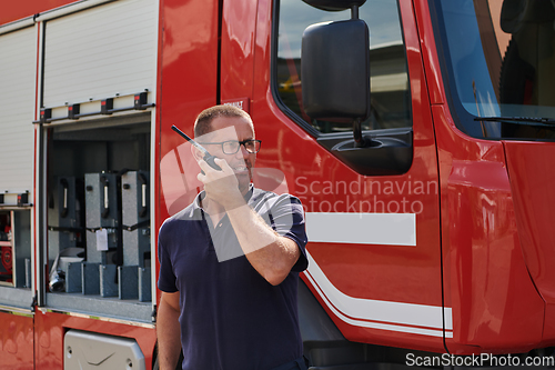 Image of A dedicated firefighter, captured in a moment of communication, stands before a modern firetruck, showcasing the seamless integration of technology in emergency response