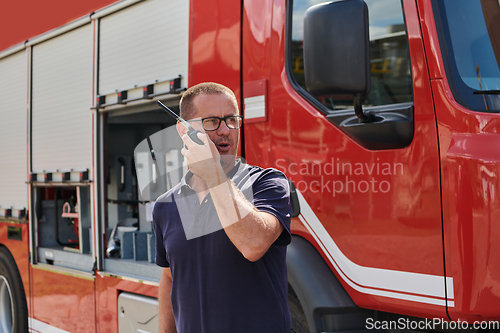 Image of A dedicated firefighter, captured in a moment of communication, stands before a modern firetruck, showcasing the seamless integration of technology in emergency response