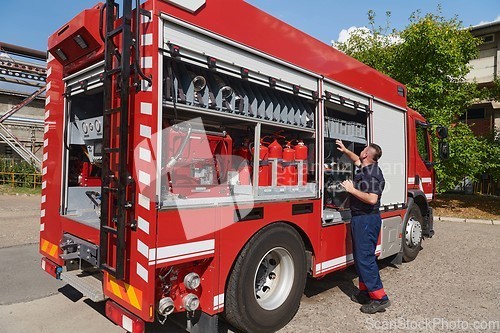 Image of A dedicated firefighter preparing a modern firetruck for deployment to hazardous fire-stricken areas, demonstrating readiness and commitment to emergency response