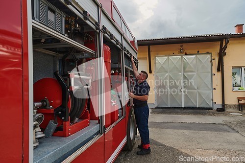 Image of A dedicated firefighter preparing a modern firetruck for deployment to hazardous fire-stricken areas, demonstrating readiness and commitment to emergency response