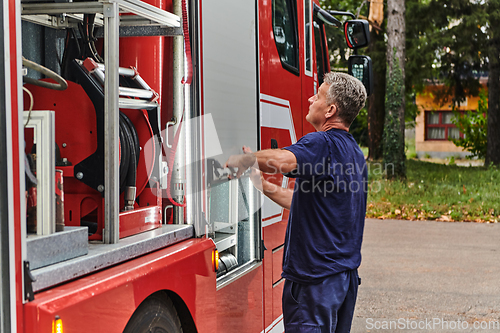 Image of A dedicated firefighter preparing a modern firetruck for deployment to hazardous fire-stricken areas, demonstrating readiness and commitment to emergency response