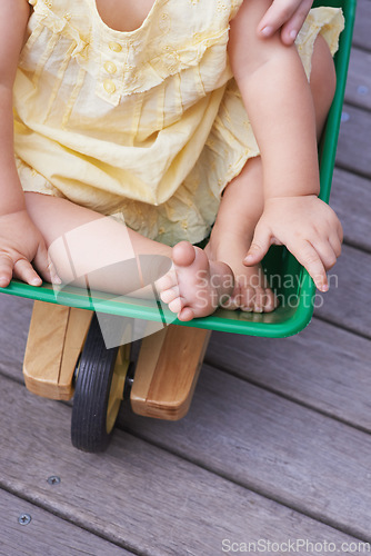 Image of Baby, child and riding toy wagon in outdoors, plastic and fun activity for childhood. Kid, toddler and wheelbarrow for playing games on porch or deck, closeup and relaxing in construction equipment