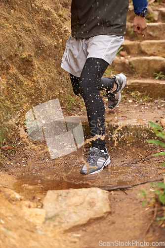 Image of Puddle, trail or legs of runner running in nature training, cardio exercise or endurance workout for wellness. Steps, splash or closeup of sports athlete on jog in a mountain outdoors for fitness