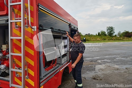 Image of A dedicated firefighter preparing a modern firetruck for deployment to hazardous fire-stricken areas, demonstrating readiness and commitment to emergency response