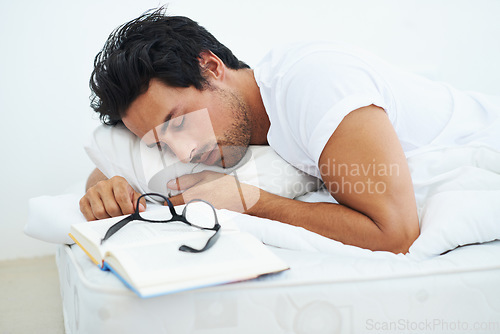 Image of Sleeping, reading and a young man in the bedroom of his home with a book to relax or rest on the weekend. Study, learning or education with a tired person asleep on a book while lying in bed