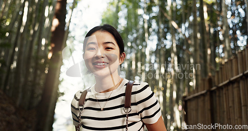 Image of Japanese woman, portrait and bamboo in forest with smile, pride and backpack for travel on holiday in bush. Girl, person and happy with hiking by plants, freedom and outdoor by trees, woods or nature