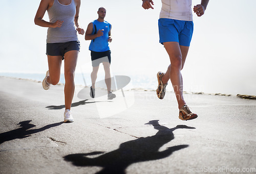 Image of People, legs and running at beach for exercise, fitness or outdoor workout together on asphalt or road. Closeup of athletic group or runners in sports, teamwork or cardio training by the ocean coast