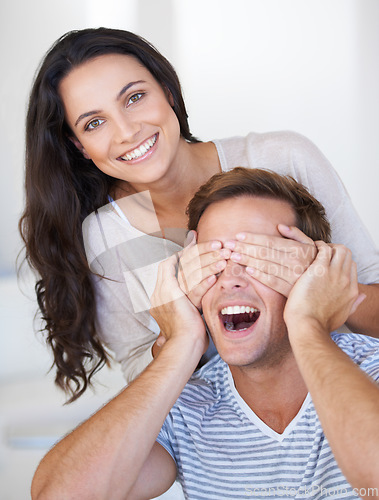 Image of Surprise, eyes and couple in house with love, affection and playful in marriage with care bonding. Woman, hands and man face for relationship fun on anniversary, together and happiness in living room