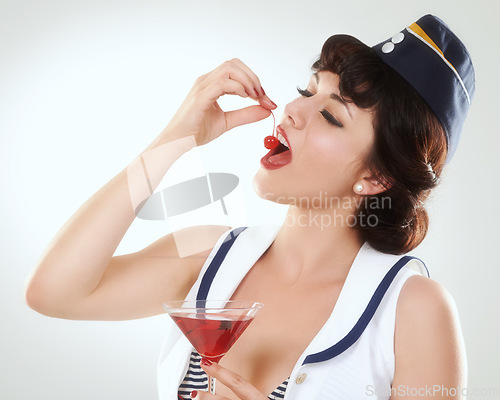 Image of Cocktail, stewardess and woman eating cherry in studio isolated on white background. Red martini, glass and air hostess enjoy alcohol fruit, vintage pin up girl or flight attendant travel on journey