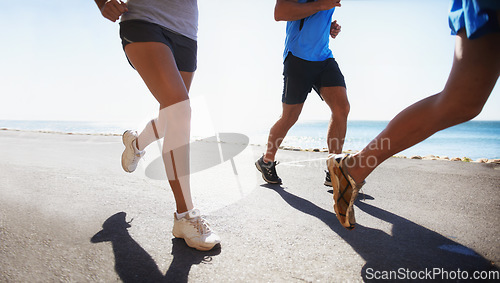 Image of People, fitness and legs running at beach for exercise or outdoor workout together on asphalt or road. Closeup of athletic group or runners in sports, teamwork or cardio training by the ocean coast