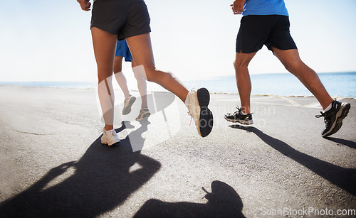 Image of People, legs and running at beach for cardio, fitness or outdoor workout together on asphalt or road. Closeup of athletic group or runners in sports, teamwork or training exercise by the ocean coast