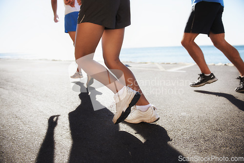 Image of People, team and legs running at beach for cardio, fitness or outdoor workout together on asphalt or road. Closeup of athletic group or runners in sports or training exercise by the ocean coast