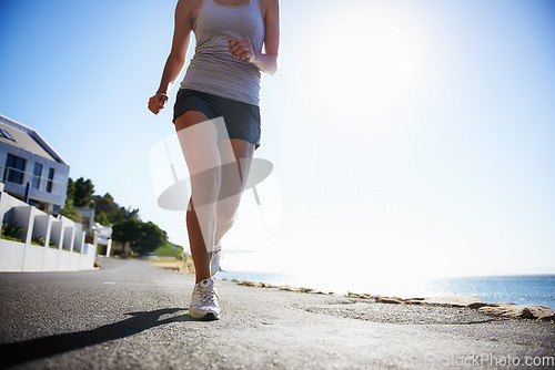 Image of Woman, running and asphalt at beach for fitness, workout or outdoor cardio training on a sunny day. Closeup of athlete legs on run, sprint or race on road or street by the ocean coast on mockup space