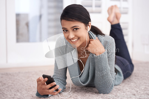 Image of Portrait of happy woman on floor with phone, earphones and relax with mobile app for podcast in house. Face of girl lying on carpet with smile, music and streaming service fon smartphone in home.