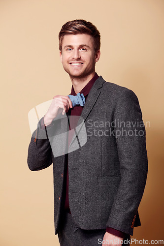 Image of Portrait, fashion and smile with a young man in studio on a tan background to wear a trendy bowtie. Happy, style and clothes with a confident model in a retro or vintage suit for a formal event